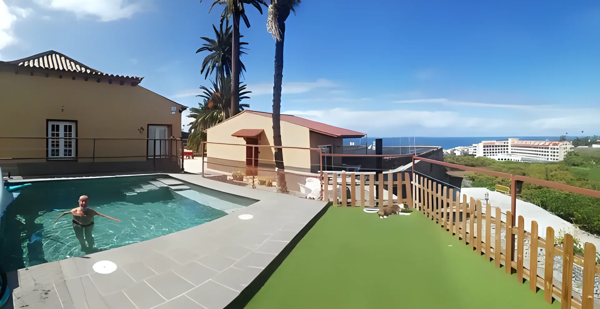 Piscina exterior de Finca las Tapias con césped, palmeras y vistas al mar de Puerto de la Cruz
